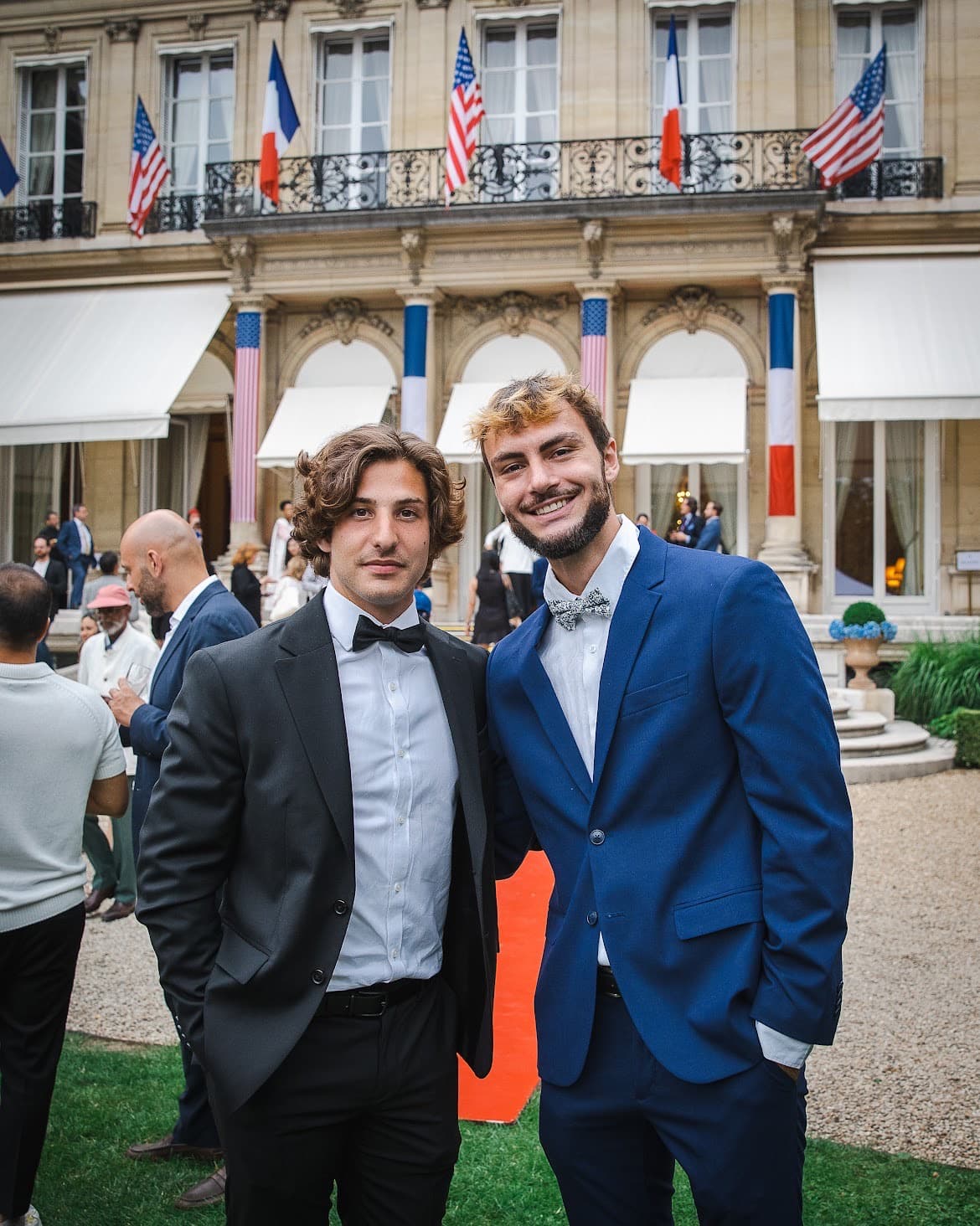 Alex Durand and Tom Carles in suits, French and American flags behind them